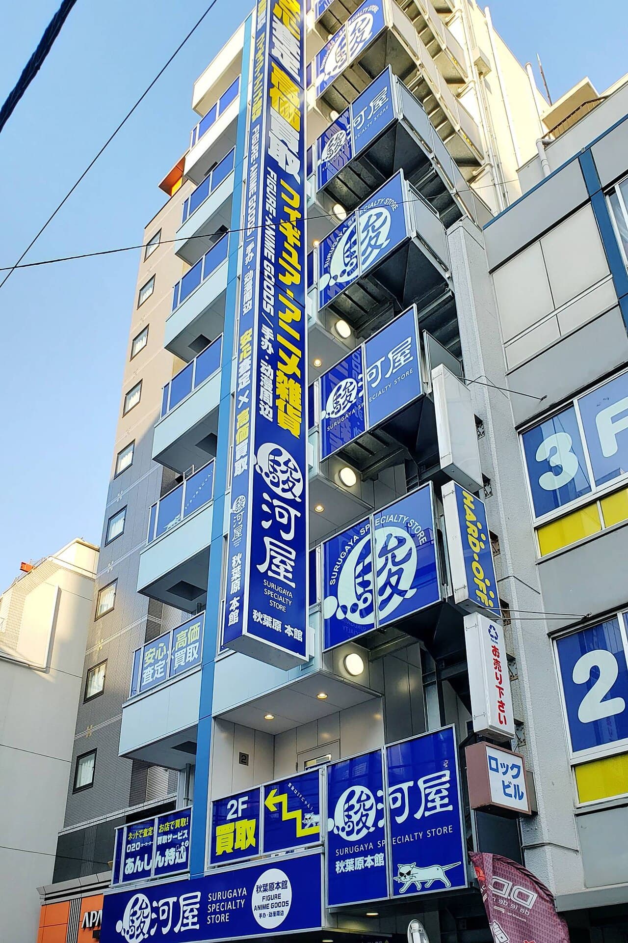 The tower of blue "Surugaya Specialty Store / Akihabara Honkan" signage on the exterior of Surugaya Akihabara Main Store, on Akihabara's Junk Alley