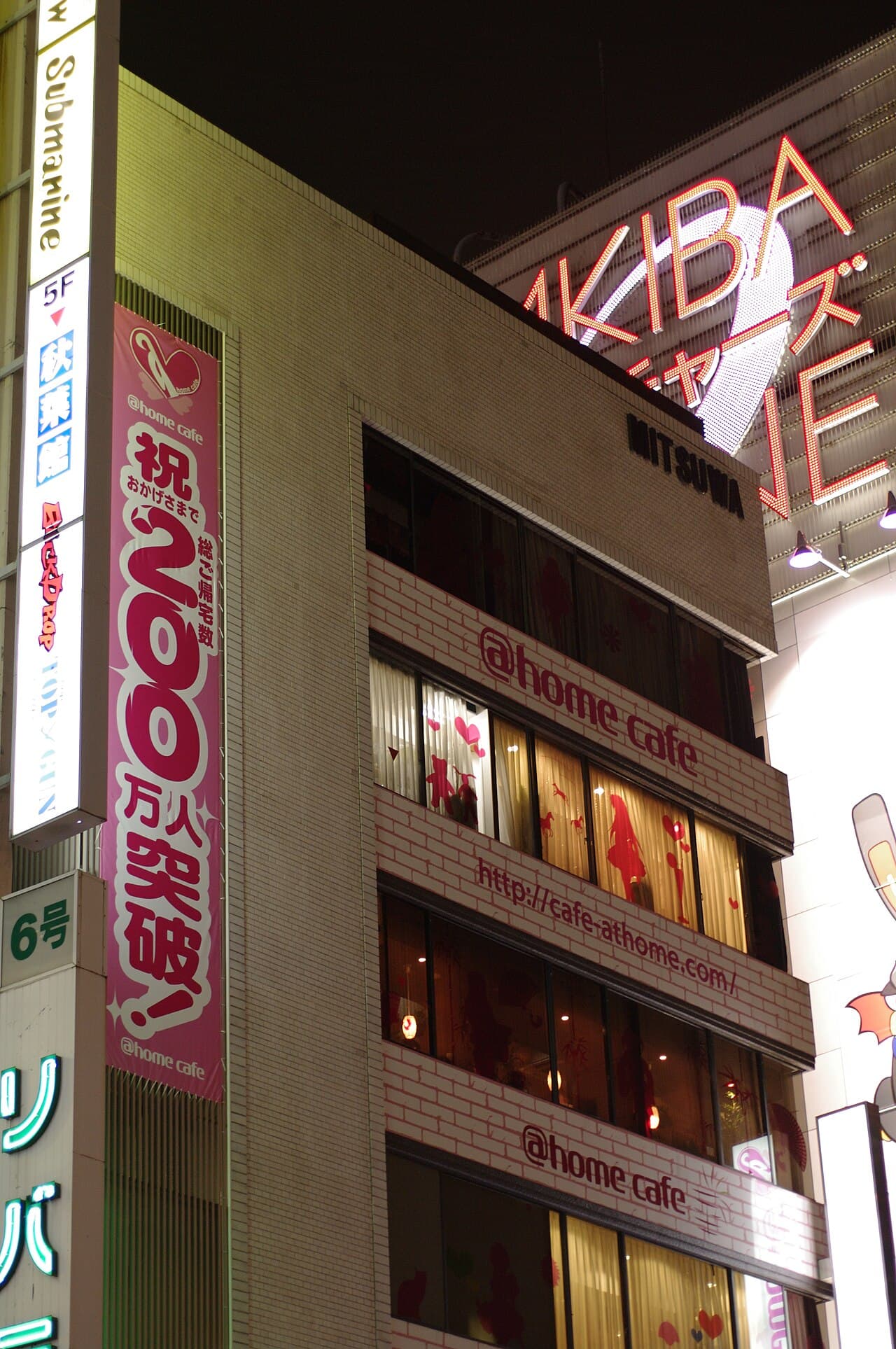 The Mitsuwa Building at night, its upper floors wrapped in "@home cafe" signage (cafe-athome.com) — the maid cafe's Akihabara home