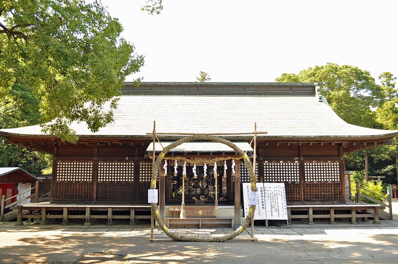 The wooden worship hall (haiden) of Washinomiya Shrine in Kuki, Saitama, fronted by a large chinowa straw ring set up for the summer purification rite — one of Japan's most famous anime-pilgrimage (seichi junrei) sites, the real-life model for Lucky Star.
