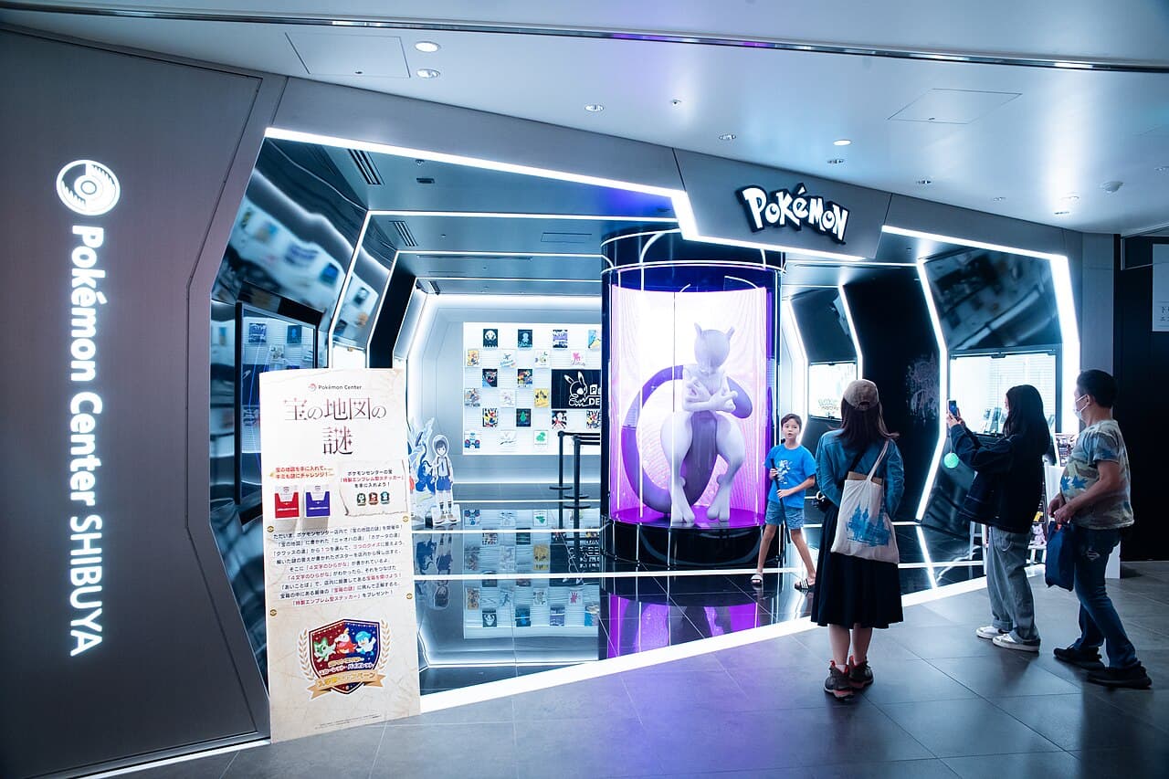 Visitors at the entrance of Pokémon Center Shibuya on Shibuya PARCO 6F, where the life-size Mewtwo statue glows purple in its illuminated capsule.