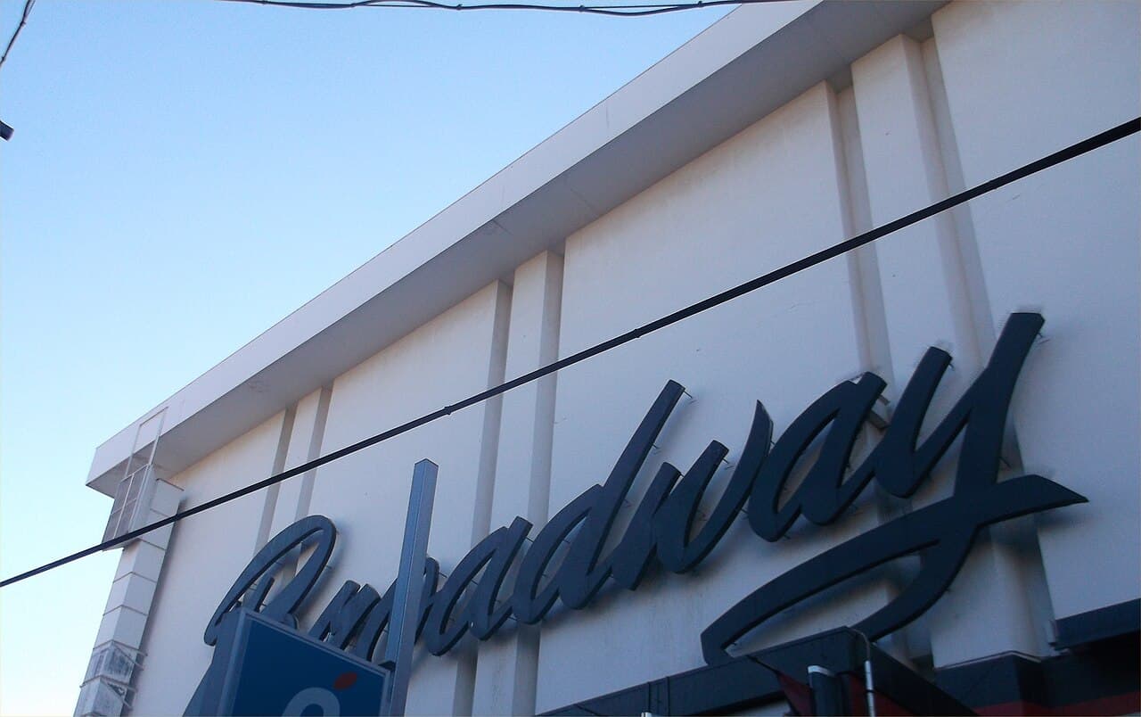 Exterior facade of the Nakano Broadway shopping complex in Nakano, Tokyo, with its large cursive "Broadway" sign on the white building, seen from below against an evening sky.