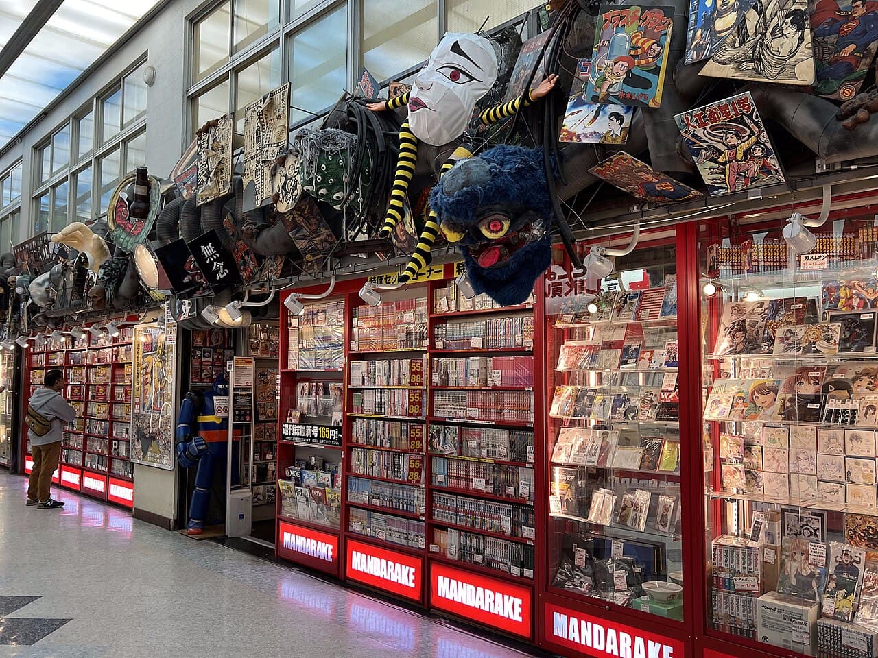The red-signed Mandarake main store lines an interior corridor of Nakano Broadway in Tokyo, its glass cases packed with vintage manga and collectibles.