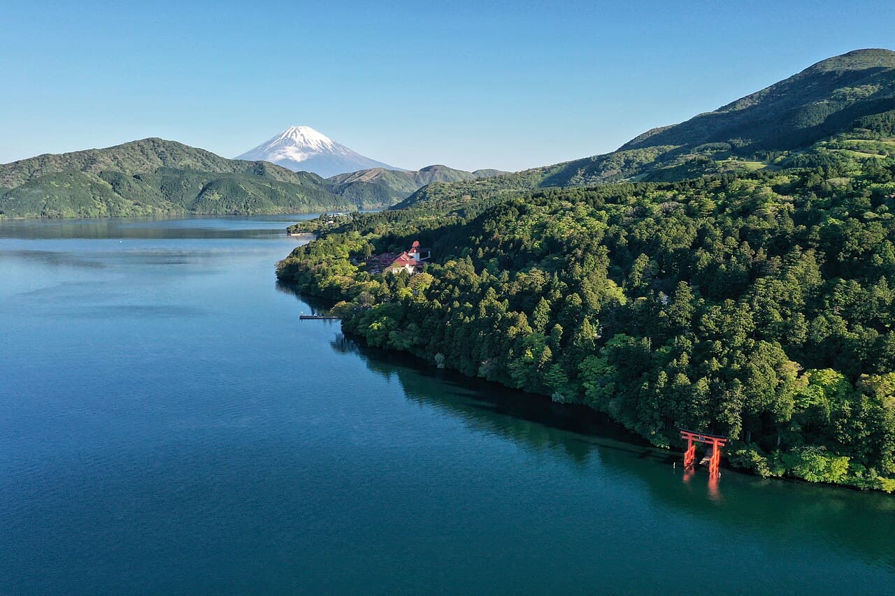 Aerial view of Lake Ashi in Hakone with snow-capped Mount Fuji in the distance and the red Hakone Shrine torii gate standing in the water